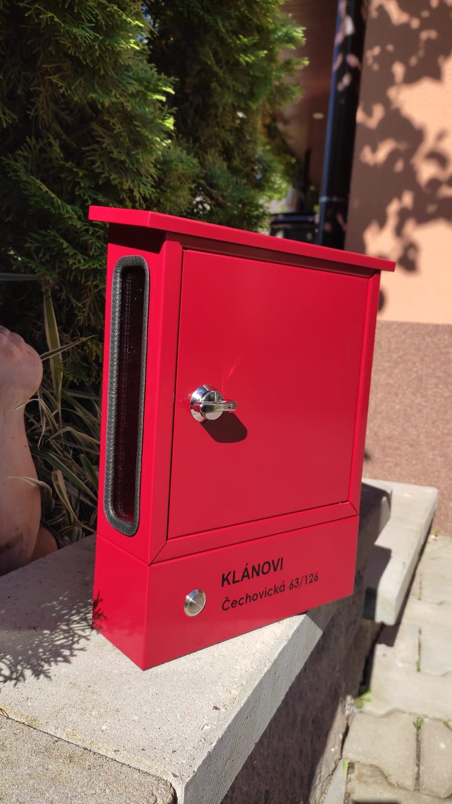 Červená poštovní schránka se zvonkem a průhledem.
